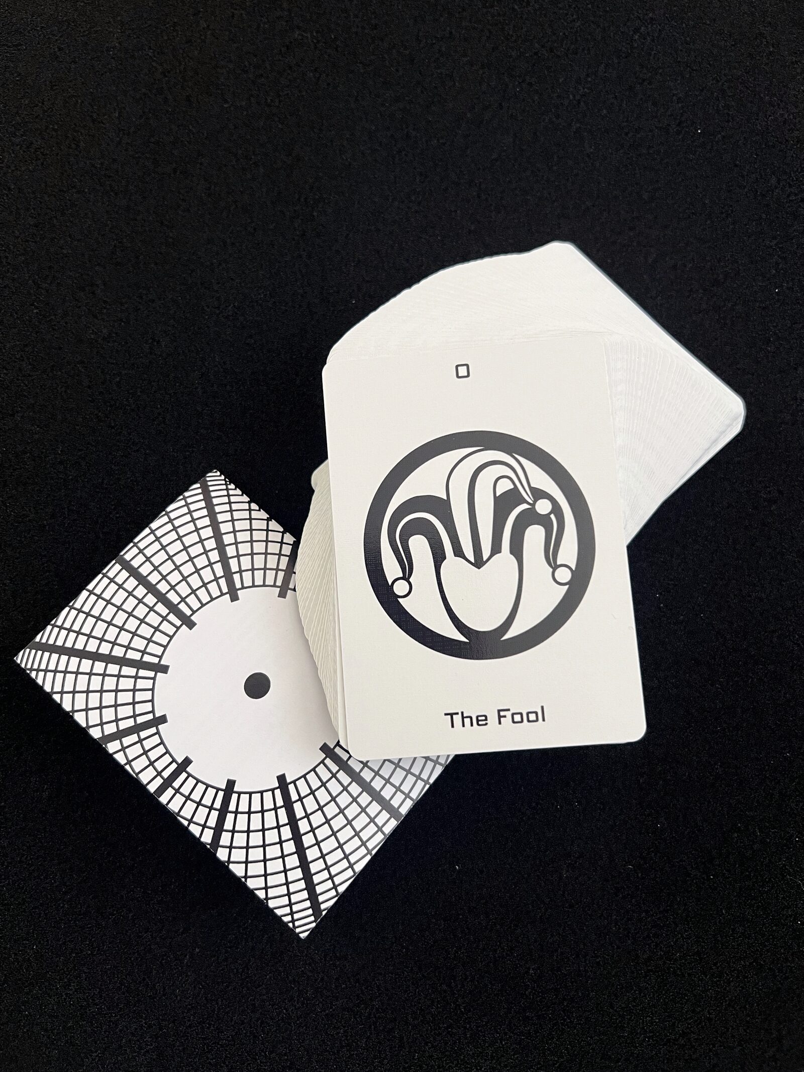 The Fool card from the Ikonology tarot deck, drawn as a jester's cap icon, beside the clock-face card back
